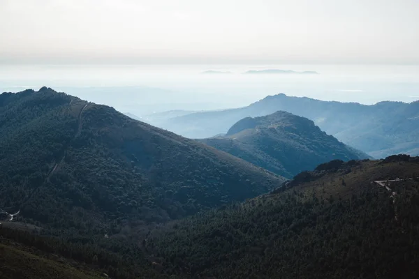 Las Villuercas, Cceres 'te sisli bir sabahta ağaçlarla kaplı mavi dağ tabakalarıyla manzara