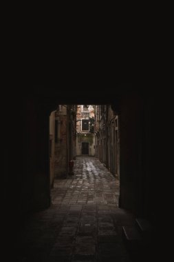 Venedik 'in dar bir sokağında loş ışıklı, gölgeli bir taş sokak, bulutlu bir günde, uzaklarda bir yangın musluğu var..