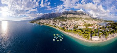 Hırvatistan 'ın Makarska kentinin insansız hava görüntüsü. Şehrin üzerinde gün batımı, sahil ve sette. Arka planda Biokovo dağları var. Yaz zamanı..