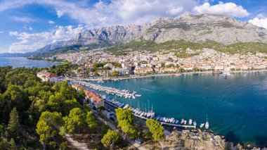 Hırvatistan 'ın Makarska kentinin insansız hava görüntüsü. Şehrin üzerinde gün batımı, sahil ve sette. Arka planda Biokovo dağları var. Yaz zamanı..