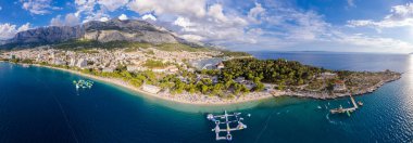 Hırvatistan 'ın Makarska kentinin insansız hava görüntüsü. Şehrin üzerinde gün batımı, sahil ve sette. Arka planda Biokovo dağları var. Yaz zamanı..