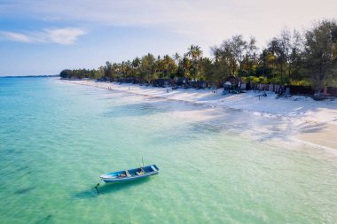 Relax on the white sand beach in Kiwengwa village on Zanzibar while admiring a Dhow catamaran sailboat gently gliding through the crystal-clear waters.
