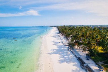 The aerial view of Zanzibar's Indian Ocean coastline is simply stunning, featuring palm trees, white sand, and sparkling blue waters. With luxurious hotels and a tropical landscape, it is the perfect destination for a summer holiday. 