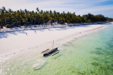 Relax on the white sand beach in Kiwengwa village on Zanzibar while admiring a Dhow catamaran sailboat gently gliding through the crystal-clear waters.