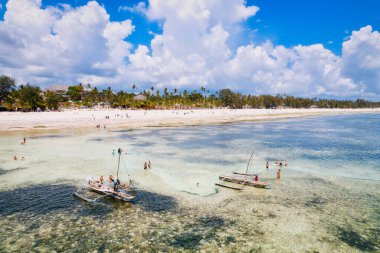 Relax on the white sand beach in Kiwengwa village on Zanzibar while admiring a Dhow catamaran sailboat gently gliding through the crystal-clear waters.