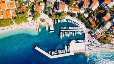 Croatia's harbor is a sight to behold from above. This breathtaking aerial view captures the colorful landscape filled with sailboats, motorboats, and luxurious yachts resting in a clear blue bay. Add this travel image to your collection of 