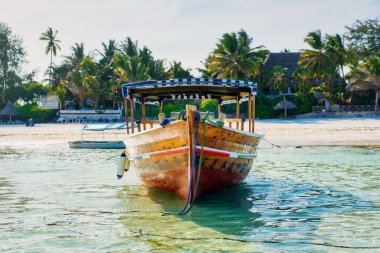 Tropik bir adanın yakınında, geleneksel bir Zanzibar balıkçı teknesi sahile yakın berrak sularda uzanıyor, yaz gezileri ve balıkçı tekneleri için mükemmel.