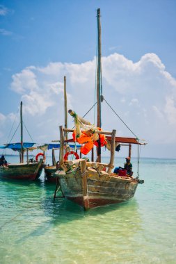 Tropik bir adanın yakınında, geleneksel bir Zanzibar balıkçı teknesi sahile yakın berrak sularda uzanıyor, yaz gezileri ve balıkçı tekneleri için mükemmel.