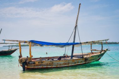 Geleneksel bir Zanzibar balıkçı teknesinin güzelliğini tecrübe edin. Tropik bir adanın sahilindeki berrak sularda dinleniyor. Yaz yolculuğu ve balıkçı tekneleri için ideal..