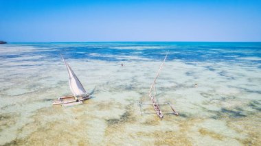 Zanzibar 'ın tropikal sahilinin güzelliğini kuş bakışı bir manzaradan, gün doğumunda kumlu sahilde dinlenen balıkçı tekneleriyle yaşayın. Yukarıdan aşağıya doğru olan perspektifte berrak mavi sular, yeşil palmiye ağaçları ve hatta bir yat bile görülüyor..