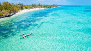 Zanzibar 'ın tropikal sahil şeridinin nefes kesen güzelliğini ele alalım. Balıkçı tekneleri güneş doğarken kumlu sahili işaretliyor. Yukarıdan bakıldığında açık mavi bir deniz, yeşil palmiye ağaçları ve hatta bir yat görünüyor..