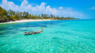 Zanzibar 'ın tropikal sahil şeridinin nefes kesen güzelliğini ele alalım. Balıkçı tekneleri güneş doğarken kumlu sahili işaretliyor. Yukarıdan bakıldığında açık mavi bir deniz, yeşil palmiye ağaçları ve hatta bir yat görünüyor..