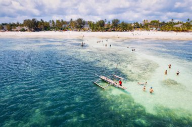 Zanzibar 'ın tropikal sahil şeridinin nefes kesen güzelliğini ele alalım. Balıkçı tekneleri güneş doğarken kumlu sahili işaretliyor. Yukarıdan bakıldığında açık mavi bir deniz, yeşil palmiye ağaçları ve hatta bir yat görünüyor..