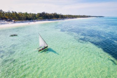Zanzibar 'ın tropikal sahil şeridinin nefes kesen güzelliğini ele alalım. Balıkçı tekneleri güneş doğarken kumlu sahili işaretliyor. Yukarıdan bakıldığında açık mavi bir deniz, yeşil palmiye ağaçları ve hatta bir yat görünüyor..