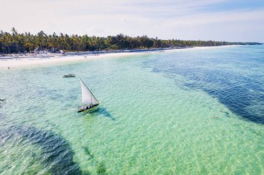 Zanzibar 'ın tropikal sahil şeridinin nefes kesen güzelliğini ele alalım. Balıkçı tekneleri güneş doğarken kumlu sahili işaretliyor. Yukarıdan bakıldığında açık mavi bir deniz, yeşil palmiye ağaçları ve hatta bir yat görünüyor..
