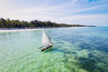 Zanzibar 'ın tropikal sahil şeridinin nefes kesen güzelliğini ele alalım. Balıkçı tekneleri güneş doğarken kumlu sahili işaretliyor. Yukarıdan bakıldığında açık mavi bir deniz, yeşil palmiye ağaçları ve hatta bir yat görünüyor..