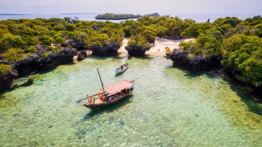 Zanzibar 'ın tropikal sahil şeridinin nefes kesen güzelliğini ele alalım. Balıkçı tekneleri güneş doğarken kumlu sahili işaretliyor. Yukarıdan bakıldığında açık mavi bir deniz, yeşil palmiye ağaçları ve hatta bir yat görünüyor..