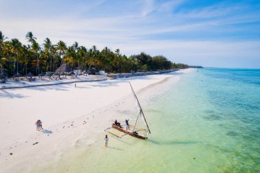 Zanzibar 'ın tropikal sahil şeridinin nefes kesen güzelliğini ele alalım. Balıkçı tekneleri güneş doğarken kumlu sahili işaretliyor. Yukarıdan bakıldığında açık mavi bir deniz, yeşil palmiye ağaçları ve hatta bir yat görünüyor..