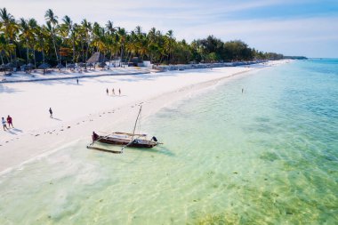 Zanzibar 'ın tropikal sahil şeridinin nefes kesen güzelliğini ele alalım. Balıkçı tekneleri güneş doğarken kumlu sahili işaretliyor. Yukarıdan bakıldığında açık mavi bir deniz, yeşil palmiye ağaçları ve hatta bir yat görünüyor..
