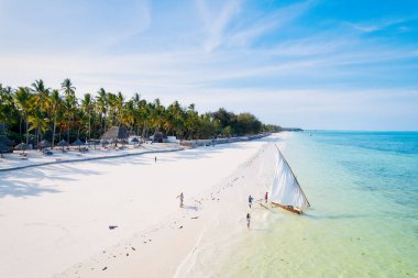 Güneşin doğuşunda kumlu sahilde dinlenen balıkçı tekneleriyle Zanzibar 'ın tropikal kıyılarının nefes kesici manzarasını ele alalım. Yukarıdan bakıldığında berrak mavi sular, yeşil palmiye ağaçları ve hatta bir yat görünüyor..