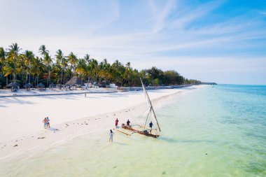 Zanzibar 'ın tropikal sahil şeridinin nefes kesen güzelliğini ele alalım. Balıkçı tekneleri güneş doğarken kumlu sahili işaretliyor. Yukarıdan bakıldığında açık mavi bir deniz, yeşil palmiye ağaçları ve hatta bir yat görünüyor..