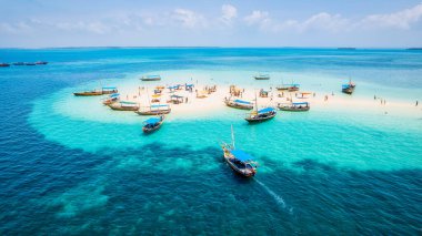 Güneşin doğuşunda kumlu sahilde dinlenen balıkçı tekneleriyle Zanzibar 'ın tropikal kıyılarının nefes kesici manzarasını ele alalım. Yukarıdan bakıldığında berrak mavi sular, yeşil palmiye ağaçları ve hatta bir yat görünüyor..