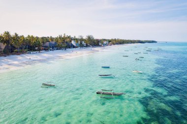 Güneşin doğuşunda kumlu sahilde dinlenen balıkçı tekneleriyle Zanzibar 'ın tropikal kıyılarının nefes kesici manzarasını ele alalım. Yukarıdan bakıldığında berrak mavi sular, yeşil palmiye ağaçları ve hatta bir yat görünüyor..