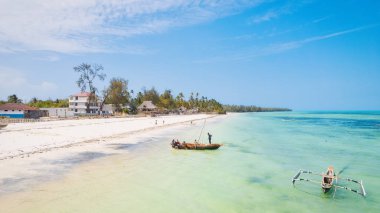 Güneşin doğuşunda kumlu sahilde dinlenen balıkçı tekneleriyle Zanzibar 'ın tropikal kıyılarının nefes kesici manzarasını ele alalım. Yukarıdan bakıldığında berrak mavi sular, yeşil palmiye ağaçları ve hatta bir yat görünüyor..