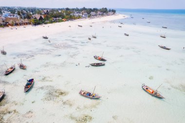 Güneşin doğuşunda kumlu sahilde dinlenen balıkçı tekneleriyle Zanzibar 'ın tropikal kıyılarının nefes kesici manzarasını ele alalım. Yukarıdan bakıldığında berrak mavi sular, yeşil palmiye ağaçları ve hatta bir yat görünüyor..