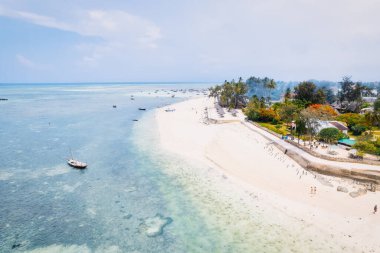 Güneşin doğuşunda kumlu sahilde dinlenen balıkçı tekneleriyle Zanzibar 'ın tropikal kıyılarının nefes kesici manzarasını ele alalım. Yukarıdan bakıldığında berrak mavi sular, yeşil palmiye ağaçları ve hatta bir yat görünüyor..