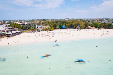 Zanzibar 'ın tropikal kıyı şeridinin havadan görünüşü güneş doğarken kumlu sahilde dinlenen balıkçı teknelerinin huzurlu görüntüsünü yakalar. Manzarada berrak mavi sular, bereketli palmiye ağaçları ve uzakta bir yat bulunur..