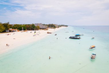 Güneşin doğuşunda kumlu sahilde dinlenen balıkçı tekneleriyle Zanzibar 'ın tropikal kıyılarının nefes kesici manzarasını ele alalım. Yukarıdan bakıldığında berrak mavi sular, yeşil palmiye ağaçları ve hatta bir yat görünüyor..