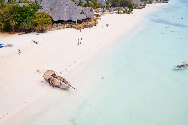 Zanzibar 'ın tropikal kıyı şeridinin havadan görünüşü güneş doğarken kumlu sahilde dinlenen balıkçı teknelerinin huzurlu görüntüsünü yakalar. Manzarada berrak mavi sular, bereketli palmiye ağaçları ve uzakta bir yat bulunur..