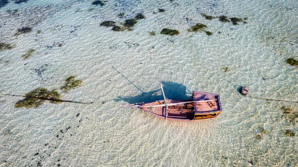 Zanzibar 'ın tropikal kıyı şeridinin havadan görünüşü güneş doğarken kumlu sahilde dinlenen balıkçı teknelerinin huzurlu görüntüsünü yakalar. Manzarada berrak mavi sular, bereketli palmiye ağaçları ve uzakta bir yat bulunur..