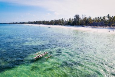 Güneşli bir yaz gününde, bulutları kabarık, güzel mavi bir gökyüzüne karşı uzanan Zanzibar Adası 'nın tropikal plajı görülmeye değer bir manzaradır. Beyaz kum, palmiye ağaçları ve kristal berraklığında turkuaz sular birleşerek rahatlatıcı bir zemin oluşturuyor. 