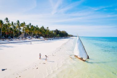 Güneşli bir yaz gününde, bulutları kabarık, güzel mavi bir gökyüzüne karşı uzanan Zanzibar Adası 'nın tropikal plajı görülmeye değer bir manzaradır. Beyaz kum, palmiye ağaçları ve kristal berraklığında turkuaz sular birleşerek rahatlatıcı bir zemin oluşturuyor. 