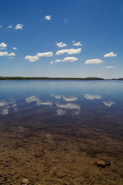 Bulutlar su manzarası fotoğrafına yansıyor. Arka planda göl kıyısı olan güzel doğa fotoğrafçılığı. Idyllic sahne. Duvar kağıdı, seyahat günlüğü, dergi, makale için yüksek kaliteli resim
