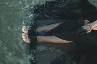 Kadın bacakları konsept fotoğrafını kapat. Güzel siyah elbise. Arka planda deniz gelgiti olan güzel sanat fotoğrafçılığı. Duvar kağıdı, seyahat günlüğü, dergi, makale için yüksek kaliteli resim