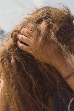Kahverengi saçlı kadın konsept fotoğrafını kapat. Saçına dokunan kadın. Güneşli bir gün. Arka planda mavi gökyüzü olan yan görüntü fotoğrafçılığı. Duvar kağıdı, seyahat günlüğü, dergi, makale için yüksek kaliteli resim