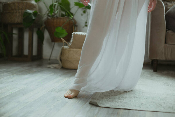 Close up bride bare foot concept photo. White wedding dress. Side view photography with cozy interior on background. High quality picture for wallpaper, travel blog, magazine, article