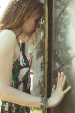 Kirli pencere manzaralı fotoğrafçılığa bakan bir kız. Arka planda terk edilmiş serası olan genç bir kadın resmi. Yüksek kalite duvar kağıdı. Reklamlar için fotoğraf konsepti, seyahat blogu, dergi, makale