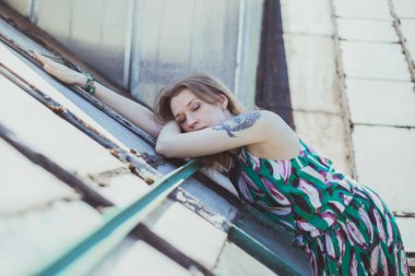 Kapalı gözlü bir kadın pejmürde çatı manzarası fotoğrafçılığının üzerinde yatıyor. Bulanık şehir manzaralı bir resim. Yüksek kalite duvar kağıdı. Reklamlar için fotoğraf konsepti, seyahat blogu, dergi, makale