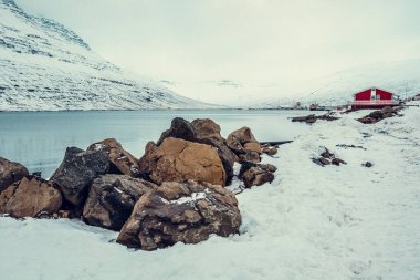 Karlı nehir manzaralı kayalar. Arka planda dağ ve kulübe olan güzel doğa fotoğrafçılığı. Idyllic sahne. Duvar kağıdı, seyahat günlüğü, dergi, makale için yüksek kaliteli resim