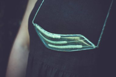 Kapalı bayan, şeffaf kolye ve kuru sivri uçlu konsept fotoğraf sunuyor. Koyu arkaplanı olan yan görüş fotoğrafçılığı. Duvar kağıdı, seyahat günlüğü, dergi, makale için yüksek kaliteli resim