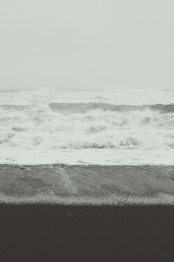 Siyah sahilin tek renkli manzarasında köpüklü dalgalar. Arka planda sis olan güzel doğa manzarası fotoğrafçılığı. Idyllic sahne. Duvar kağıdı, seyahat günlüğü, dergi, makale için yüksek kaliteli resim