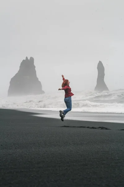 レイニスフィヤラ黒ビーチの風光明媚な写真に女性ジャンプします 背景に列の崖と人の写真 高品質の壁紙 旅行ブログ 記事のための写真のコンセプト — ストック写真