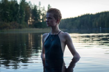 Close up short haired model in river at sunset portrait picture. Closeup side view photography with pine forest on background. High quality photo for ads, travel blog, magazine, article