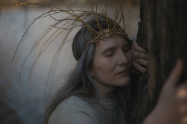 Close up ancient celtic styled woman hugging tree and praying portrait picture. Closeup side view photography with blurred background. High quality photo for ads, travel blog, magazine, article