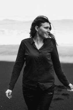 Joyful lady on black Iceland beach monochrome scenic photography. Picture of person with rough sea on background. High quality wallpaper. Photo concept for ads, travel blog, magazine, article