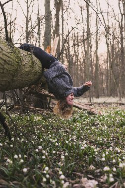 Laughing woman hanging on fallen tree scenic photography. Picture of person with wild wood on background. High quality wallpaper. Photo concept for ads, travel blog, magazine, article